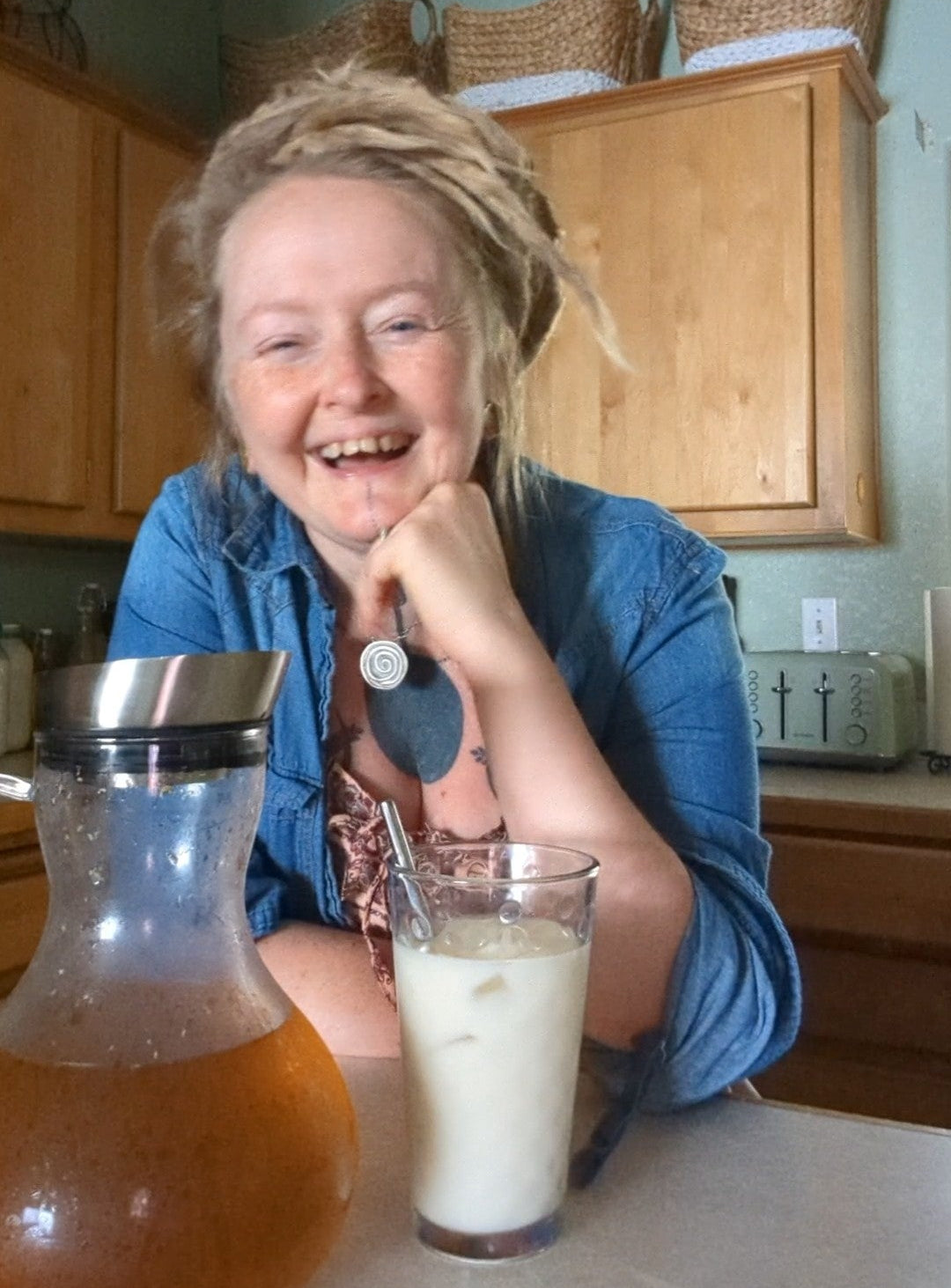 Person sitting at a kitchen counter with a glass of milk and a carafe, smiling.